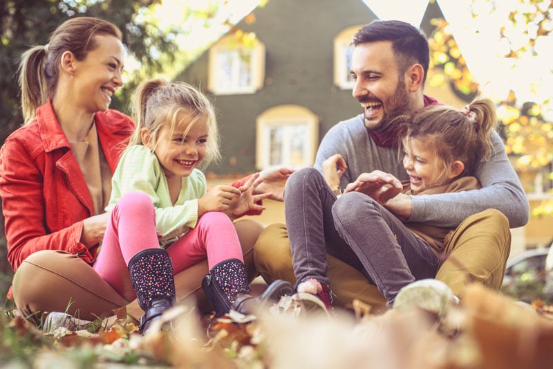 Family Of Four On Front Yard Leaf Pile Fall